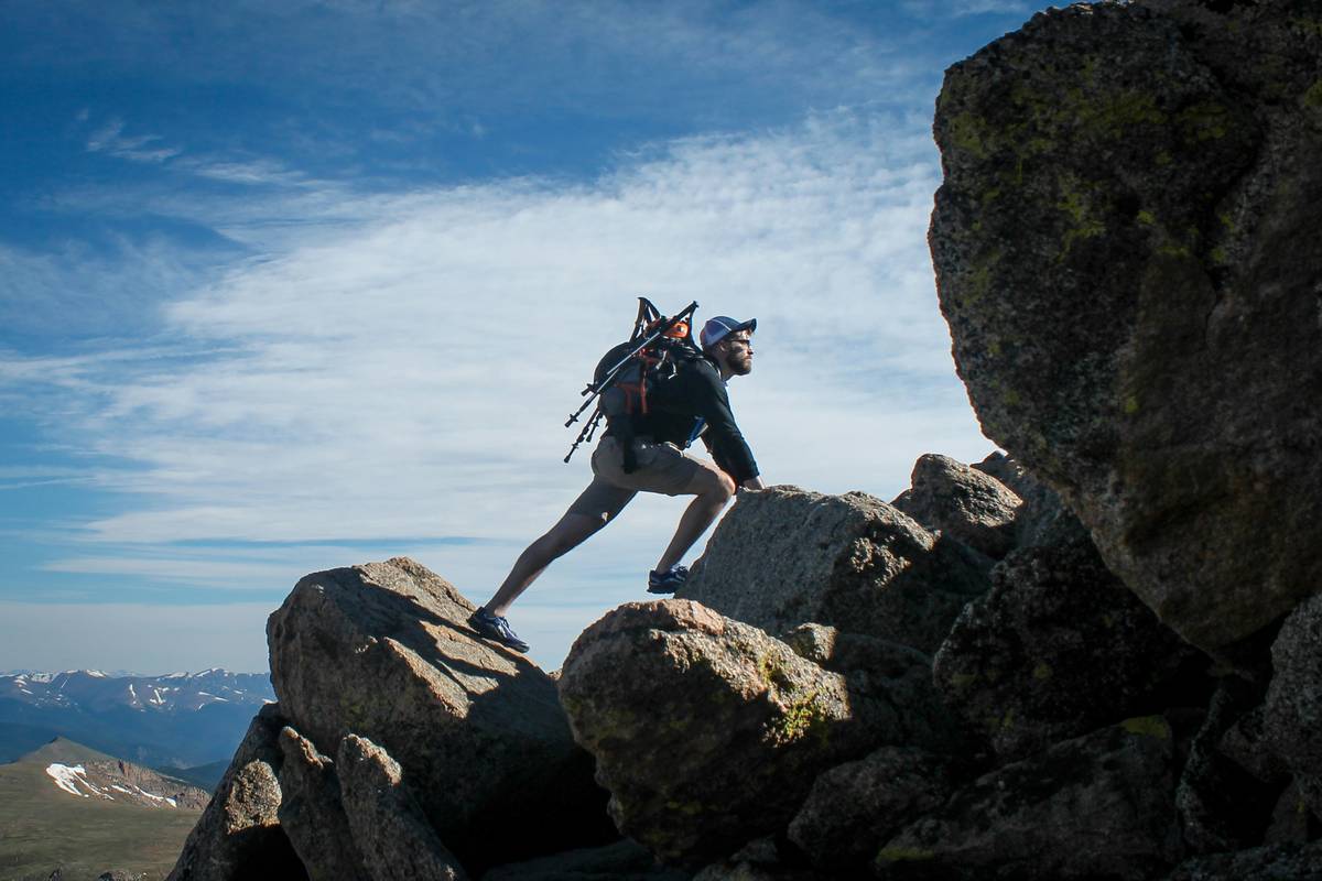 Climber wearing summit helmet guard on exposed ridge with falling debris nearby