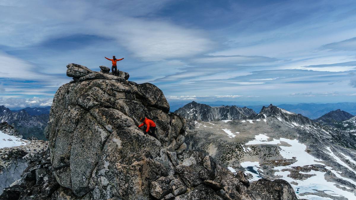 Climber wearing climbing helmet summit on snowy ridge with mountains in background
